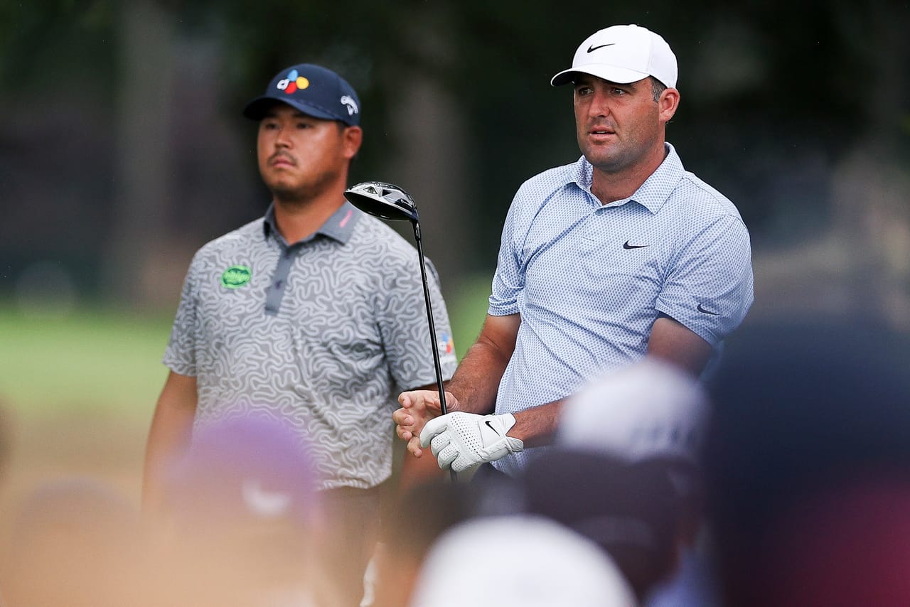 Scottie Scheffler, driver in hand, watches a tee shot with Si Woo Kim standing behind him