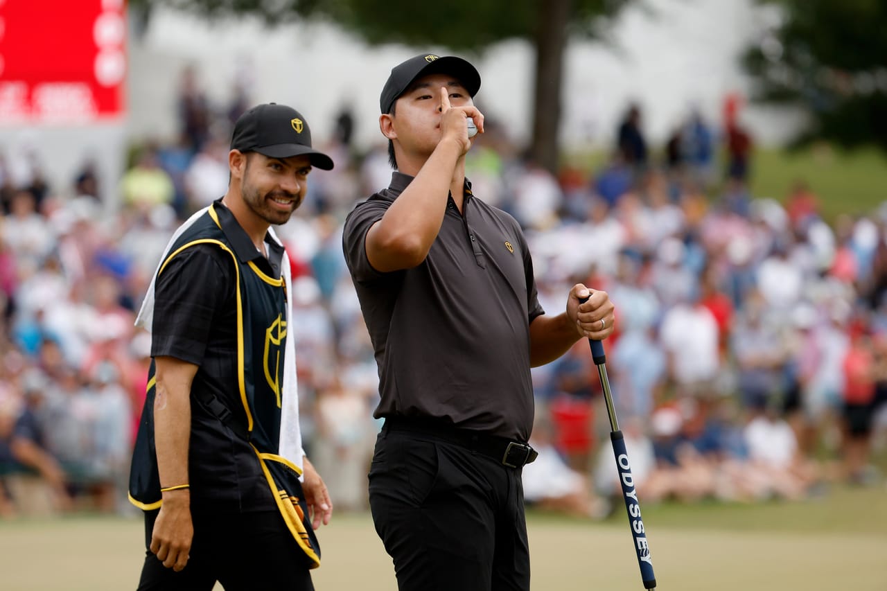 Si Woo Kim holds a finger to his lips toward the gallery on the 15th green at Quail Hollow as his caddie, Manuel Villegas, grins beside him
